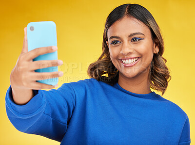 Buy stock photo Selfie, social media and smile with a woman on a yellow background in studio posing for a profile picture. Face, photograph and a happy young influencer indoor to update a status on her timeline