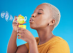 Woman, blowing bubbles and fun in studio, blue background or party celebration with fun, liquid soap or toy. African girl, person and relax with happy, joyful or creative bubble for calm break