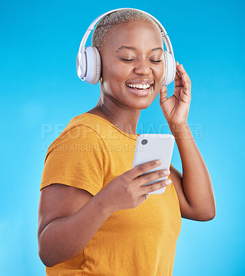 Buy stock photo Woman, phone and headphones for music, listening to audio and social media influencer on a blue background. Young african person on mobile, video streaming subscribe and radio or selfie in studio