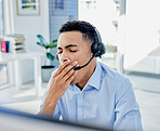 Tired, yawn and a man in a call center for customer service or support while working online at his desk. Contact us, consulting and crm with an exhausted young male employee in a telemarketing office