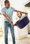 Child, father and playing in laundry basket at home for family fun and housework or cleaning. A man laughing and swinging a funny toddler kid while together for bonding, game and development at house