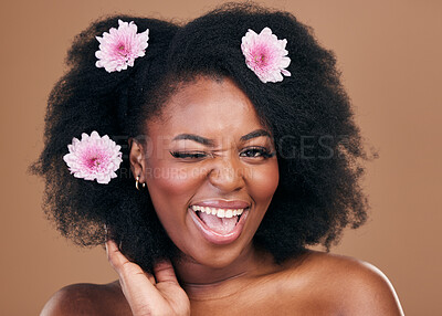 Buy stock photo Flowers, face wink and black woman in afro hair care, excited and beauty in studio isolated on a brown background. Portrait, floral hairstyle cosmetic and natural African model flirt in organic salon