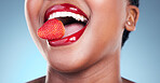 Woman, eating and strawberry, red lipstick and beauty, makeup closeup isolated on blue background. Fruit, healthy and model in a studio with bold cosmetic product, mouth and cosmetology with shine