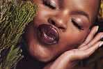 African woman, plants and lipstick in studio with kiss, beauty and wellness with natural glow by brown background. Girl, model and face with leaves, pouting or happy for cosmetics, shine or aesthetic