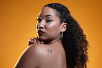 Beauty, portrait and a woman with a tattoo in studio for cosmetics, makeup and dermatology. Closeup of a young female model on an orange background in studio with body art, confidence and skin glow