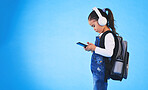 Music, backpack and child on blue background with phone ready for school, learning and education. Kindergarten, studio and young girl on with bag on smartphone for streaming song, audio and radio