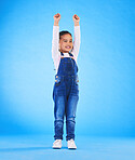 Celebration, girl child and champion, winner and achievement with happiness and excited isolated on blue background. Cheers, yes and winning with success, pride and happy kid with arms up in a studio