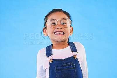 Buy stock photo Girl kid, glasses and vision in studio with smile, medical and thinking for eye care by blue background. Female child, test spectacles and young fashion model with lens, frame and excited for health