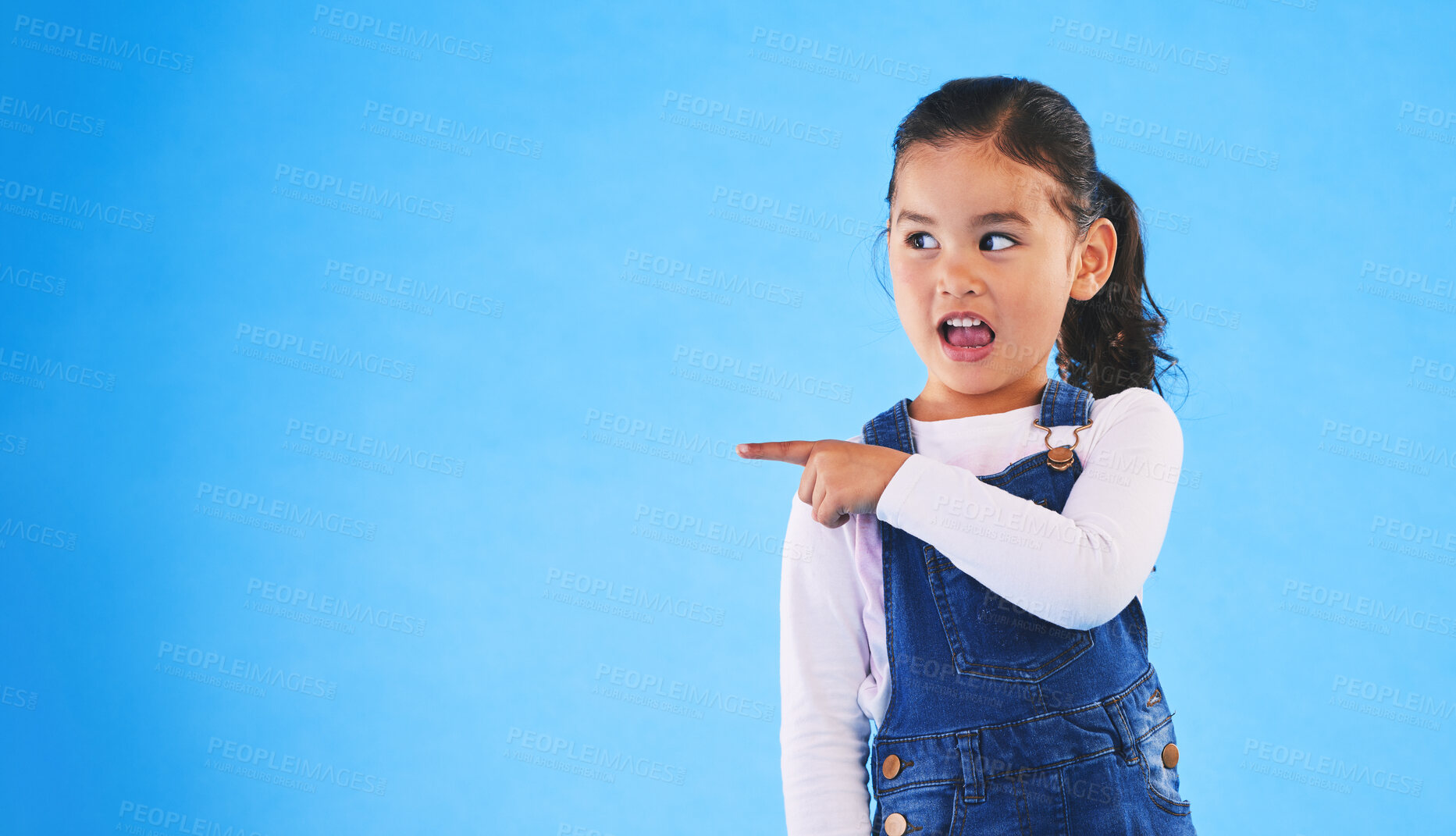 Buy stock photo Pointing, blue background and girl with mockup space for sale, advertising and promotion. Emoji, happy and young child in studio with hand gesture for discount information, announcement and news