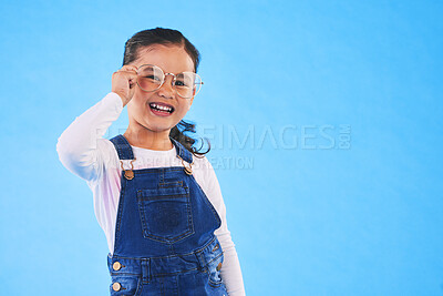 Buy stock photo Girl child, glasses and frame in studio portrait for vision, health and eye care by blue background. Female kid, test spectacles and young fashion model with lens, smile or eyesight with mockup space