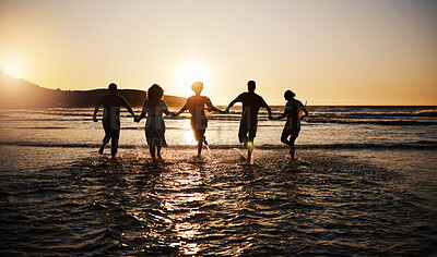 Buy stock photo Water splash, sunset and friends holding hands at a beach with freedom, running or fun vacation rear view. Ocean, silhouette and people shadow in solidarity at the sea for travel, bond or celebration