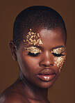 Gold flakes, beauty and black woman with face closeup with makeup and cosmetics in studio. Brown background, African female model and glitter with golden shine and glow from facial paint sparkle