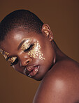 Art, glitter and black woman with gold makeup on brown background, glitter paint and cosmetics. Shine, glow and African model in studio for beauty, fashion and aesthetic freedom in luxury skincare.