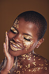 Black woman, face and gold makeup with luxury glow and skincare mask with glitter. Sparkle, smile and beauty with rich and shine of cosmetics and model in studio with facial art with brown background