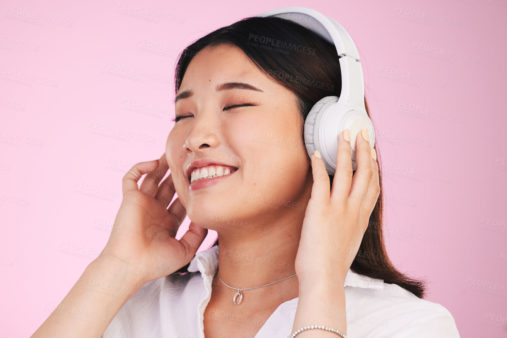 Buy stock photo Headphones, happy and young woman in a studio listening to music, playlist or album for entertainment. Smile, calm and Asian female model streaming a song or radio isolated by a pink background.