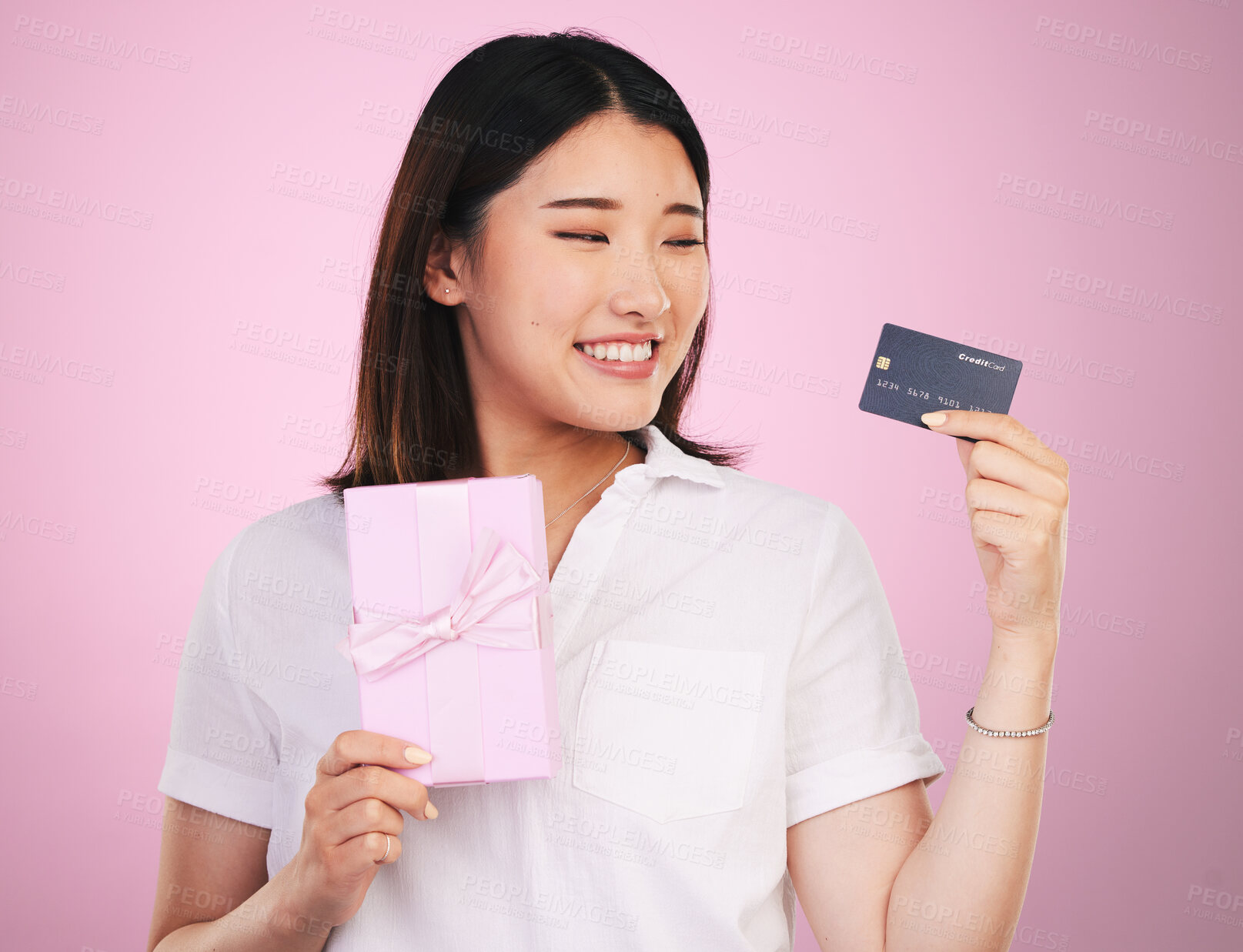 Buy stock photo Credit card, gift box and young woman in a studio online shopping a sale, discount or deal. Happy, smile and Asian female model buying a present with retail promotion isolated by a pink background.