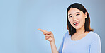 Asian woman, point and studio portrait with space, mockup and happy for promotion by blue background. Japanese student, girl and smile for review, opinion or feedback with choice, decision and sign