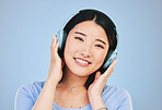 Portrait of happy Asian woman in studio with headphones for streaming radio, subscription and relax. Sound, podcast and face of person listening to music, audio and track for calm on blue background
