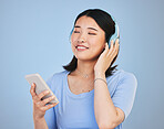 Music, headphones and happy Asian woman with phone for streaming radio, subscription and relax. Sound, online podcast and face of person listening to song, audio and track for calm on blue background