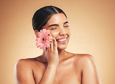 Buy stock photo Skincare, smile and woman with flower in studio for beauty, wellness and organic cosmetics on brown background. Floral, dermatology and hand on face of model happy with plant, cosmetology or results