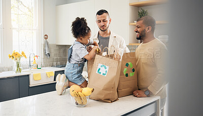 Buy stock photo Recycling, blended family or adoption with a daughter and gay couple in the home kitchen for sustainability. LGBT, eco friendly or waste with a girl and parents unpacking bananas from a grocery bag