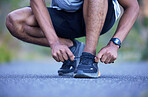 Fitness, exercise and a man tying shoelace outdoor for run, workout or training performance. Closeup of athlete person or runner with running shoes on a road for cardio or health and wellness