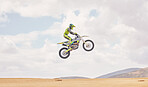 Desert, motorbike cycling and jump for sports, agile driving and off road adventure with mockup space in cloudy sky. Motorcycle, challenge and moving in air for action, fearless talent and sand dunes