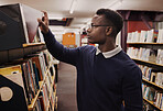 University, books and black man in a library reading and learning on campus for knowledge and education in college. Smart, clever and person doing research or studying by a shelf for an exam