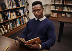 University, book and black man student reading and learning in a college for knowledge development. Serious, education and person studying research to prepare for exam or assignment in a class