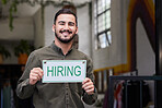 Portrait, man and we are hiring opportunity sign with recruiting, happy and smile from business owner. Male person, store and entrepreneur with recruitment poster and job search signage with manager