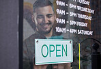 Shop, window and happy businessman open with sign for working time in retail, store or service in small business. Opening, restaurant or startup owner in Portugal with a welcome, poster and smile 