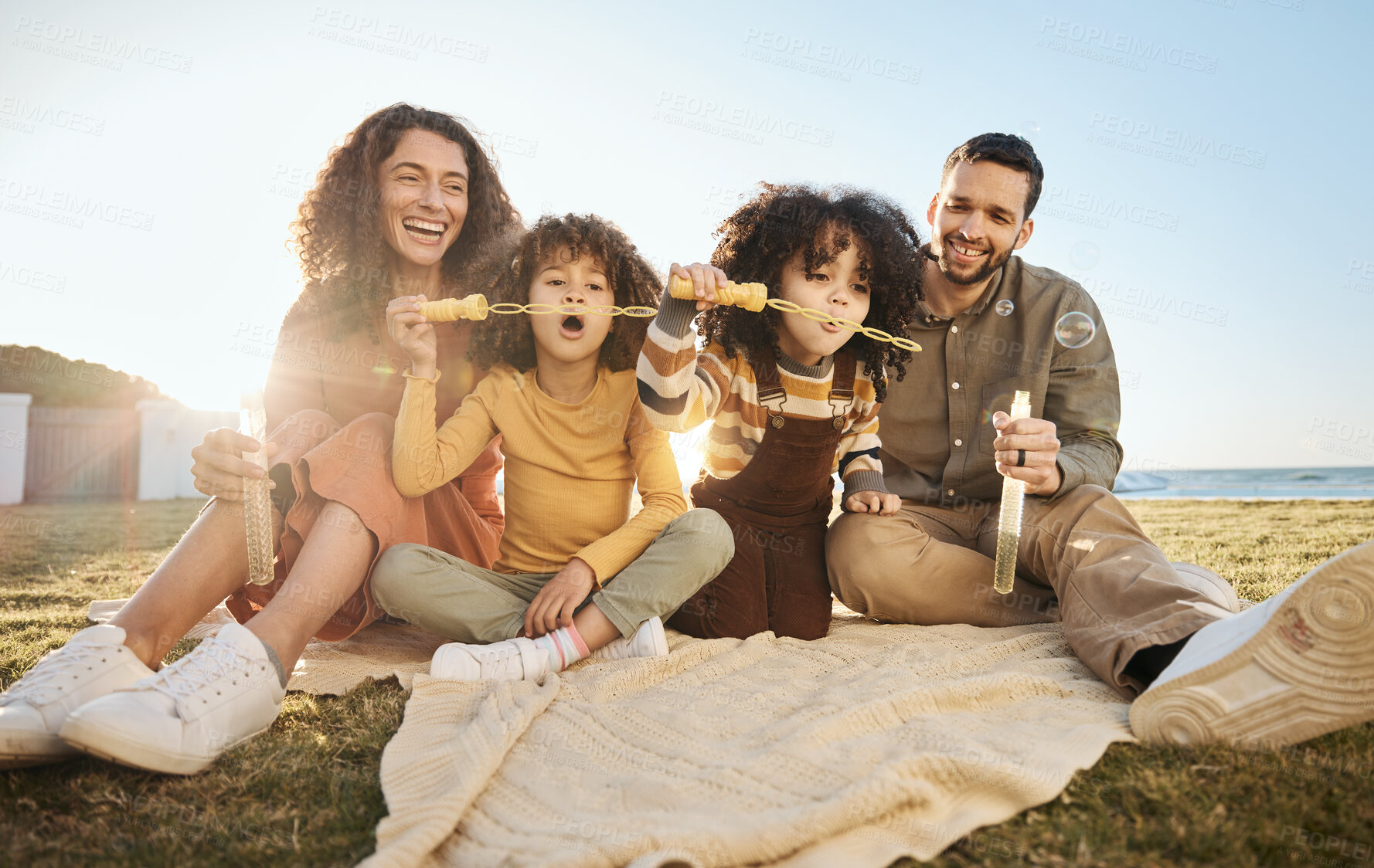 Buy stock photo Parents, children and fun bubbles at picnic at beach vacation home with smile, love and relax. Mom, dad and kids on blanket on grass with soap bubble wand, bonding ocean holiday together in summer.