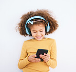 Girl kid, chat and smartphone, headphones and music with smile isolated on white background. Technology, audio streaming and social media, using phone and child with mobile app and radio in studio