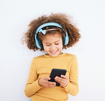 Buy stock photo Girl kid, chat and smartphone, headphones and music with smile isolated on white background. Technology, audio streaming and social media, using phone and child with mobile app and radio in studio