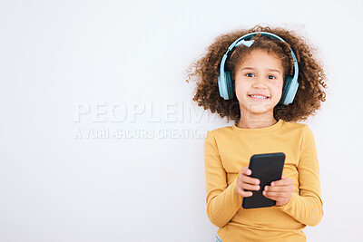 Buy stock photo Girl kid, portrait and smartphone, headphones and music with smile isolated on white background. Technology, audio streaming and social media, mockup space and child, mobile app and radio in studio