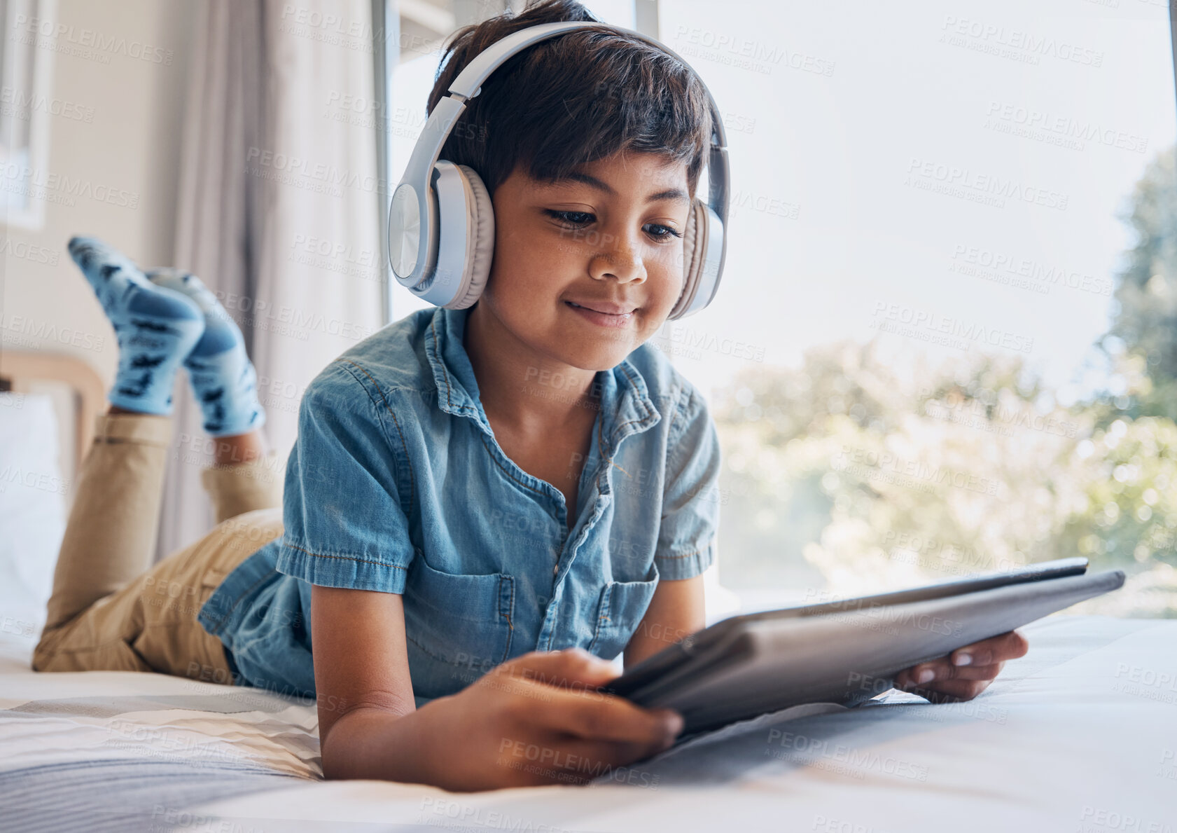 Buy stock photo Boy, tablet and headphones on bed, reading of smile for streaming subscription, movie or relax with video. Male child, digital touchscreen and thinking in bedroom for audio, show or elearning in home