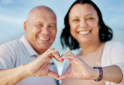 Buy stock photo Heart shape, hands and mature couple at the beach on a romantic vacation, adventure or holiday. Smile, emoji and portrait of man and woman in retirement with love or support gesture by ocean on trip.