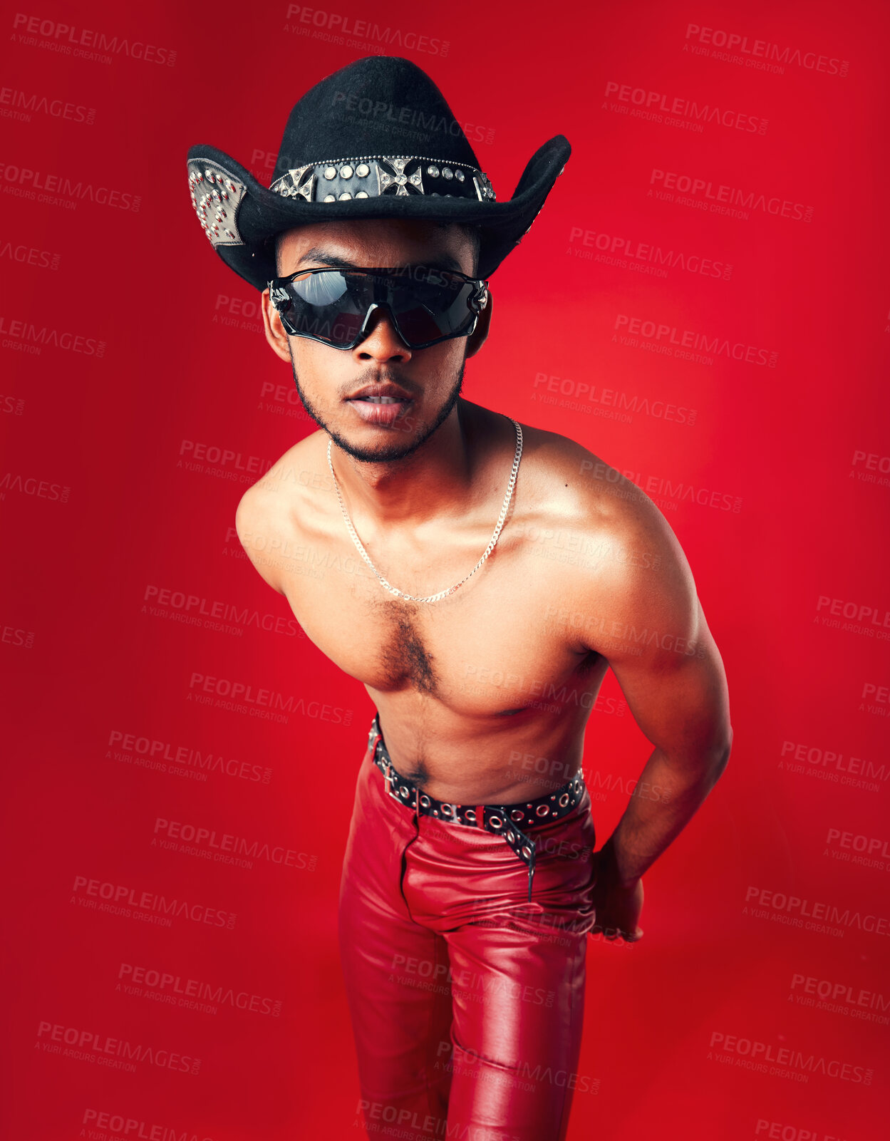 Buy stock photo Fashion, man and cowboy in hat, shirtless with sunglasses and gen z isolated on red background. Confident model, cool and leather pants with eyewear accessory, western aesthetic and edgy in studio