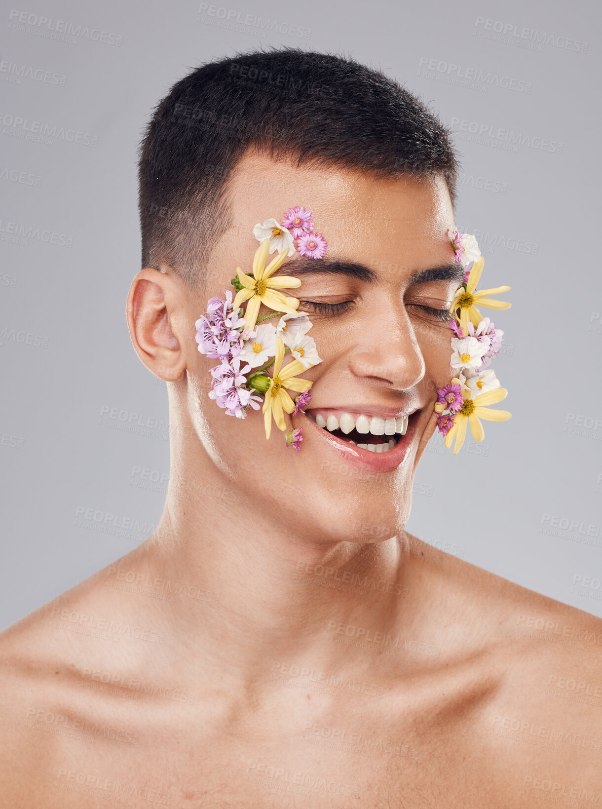 Buy stock photo Smile, skincare and a man with flowers on a studio background for creative aesthetic. Happy, plant and a male model with floral art for facial wellness and dermatology isolated on a studio backdrop