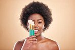 Portrait, makeup and a black woman with brushes on a studio background for wellness and foundation. Tongue out, beauty and an African person or model with product for facial cosmetics on a backdrop