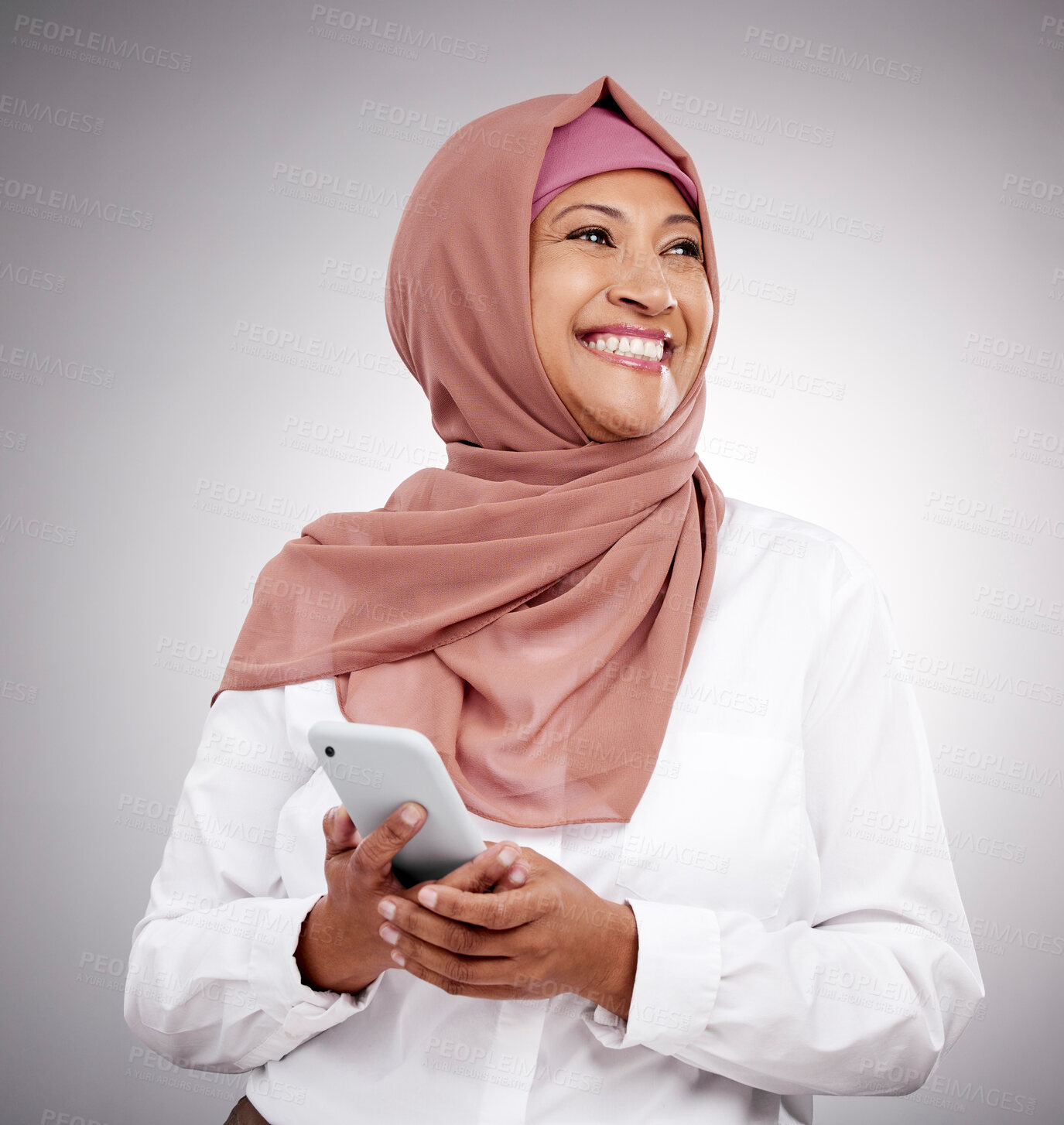 Buy stock photo Phone, happy and mature muslim woman in a studio browsing on social media, mobile app or the internet. Cellphone, thinking and islamic female model with hijab and vision isolated by a gray background