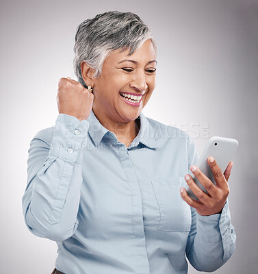 Buy stock photo Celebration, phone and senior woman in studio winning an online bet, good news or prize. Happy, fist pump and elderly female model cheering with cellphone for success isolated by gray background.