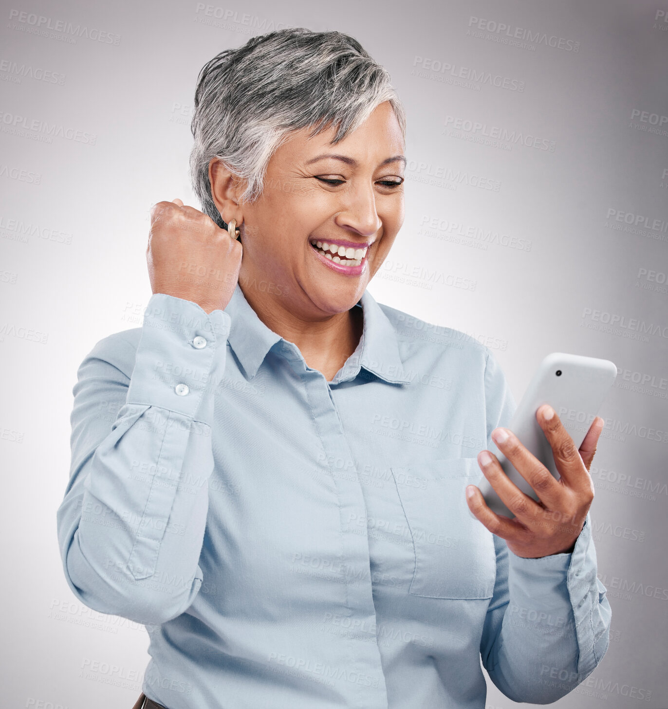 Buy stock photo Celebration, phone and senior woman in studio winning an online bet, good news or prize. Happy, fist pump and elderly female model cheering with cellphone for success isolated by gray background.