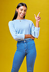 Pointing, happy and portrait of a woman in a studio for advertising, marketing or promotion. Smile, excited and young Indian female model with a direction hand gesture isolated by yellow background.
