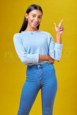 Buy stock photo Pointing, happy and portrait of a woman in a studio for advertising, marketing or promotion. Smile, excited and young Indian female model with a direction hand gesture isolated by yellow background.