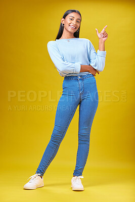 Buy stock photo Pointing, advertising and portrait of a woman in a studio for creative, marketing or promotion. Smile, happy and full length of Indian female model with a direction hand gesture by yellow background.