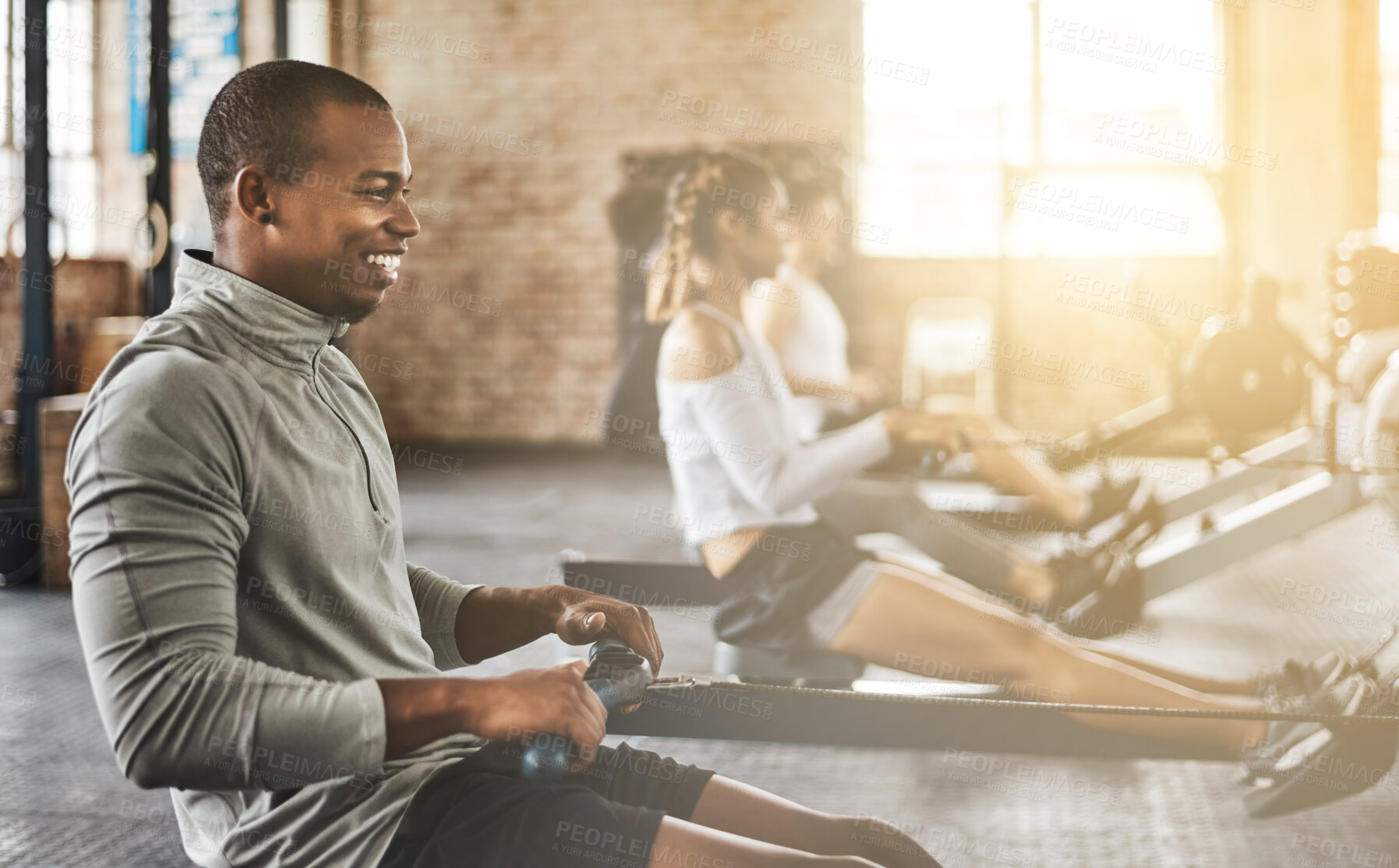 Buy stock photo Exercise, happy man and rowing machine in gym for group class, fitness workout and cardio training. African bodybuilder, athlete and challenge to row on sports equipment for energy, muscle and power