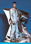 Holographic, vaporwave fashion and man with futuristic ski style with sci fi clothing in studio. Art, creative and male model with trendy, cool and cyberpunk designer clothes with blue background