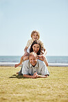 Portrait, grass and family in a pile by the ocean together for travel, vacation or holiday on a summer morning. Love, smile or happy with a father, mother and son on the ground in a stack at the sea