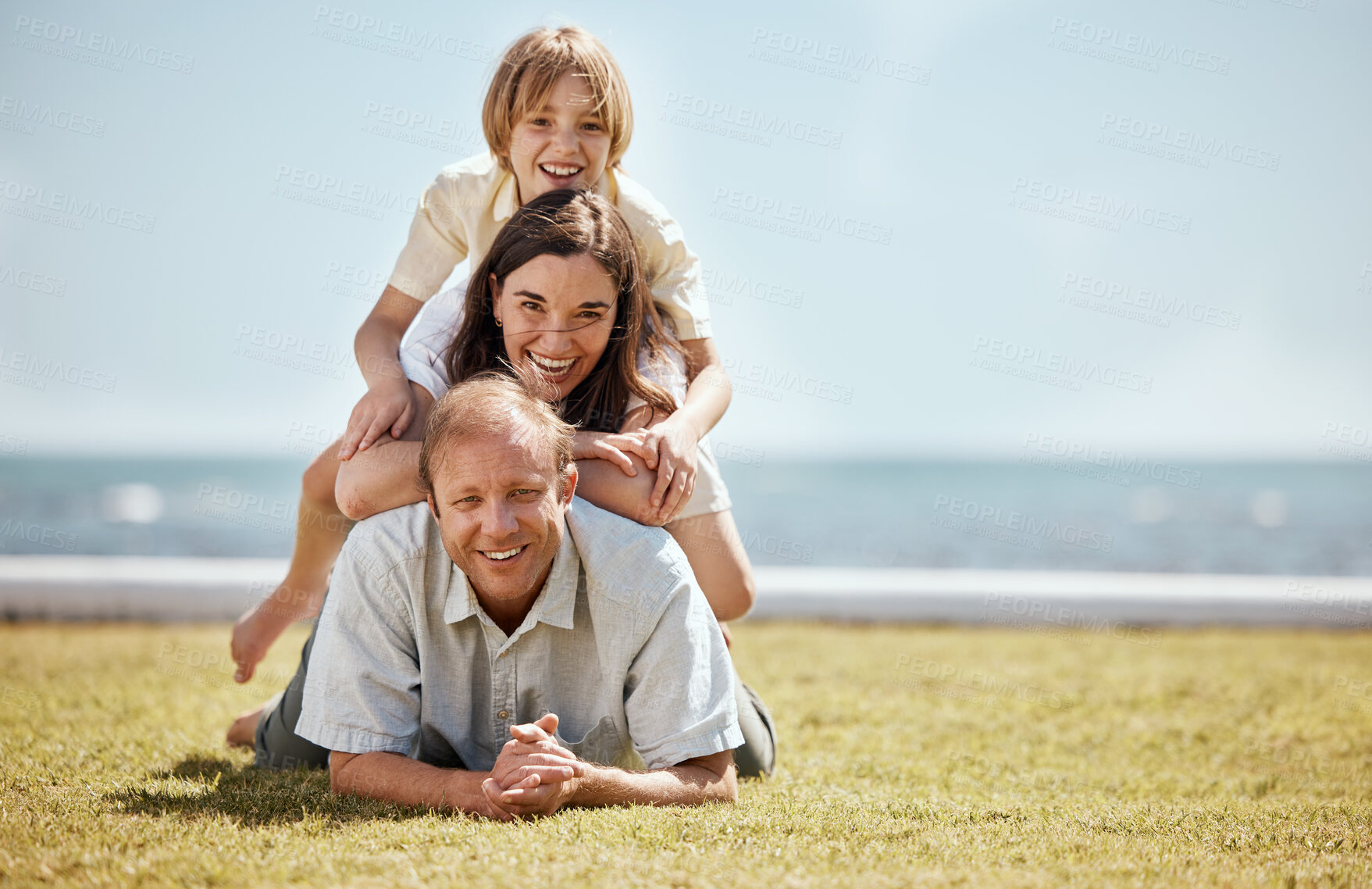 Buy stock photo Portrait, mockup and family in a pile on grass by the ocean together for travel, vacation or holiday in a summer. Love, smile or happy with a dad, mom and son on the ground in a stack at the sea